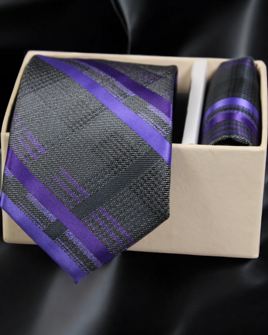 Purple and gray striped tie with matching pocket square in a box on a black background