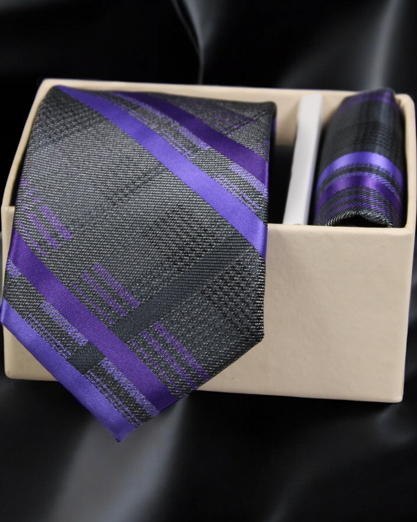 Purple and gray striped tie with matching pocket square in a box on a black background