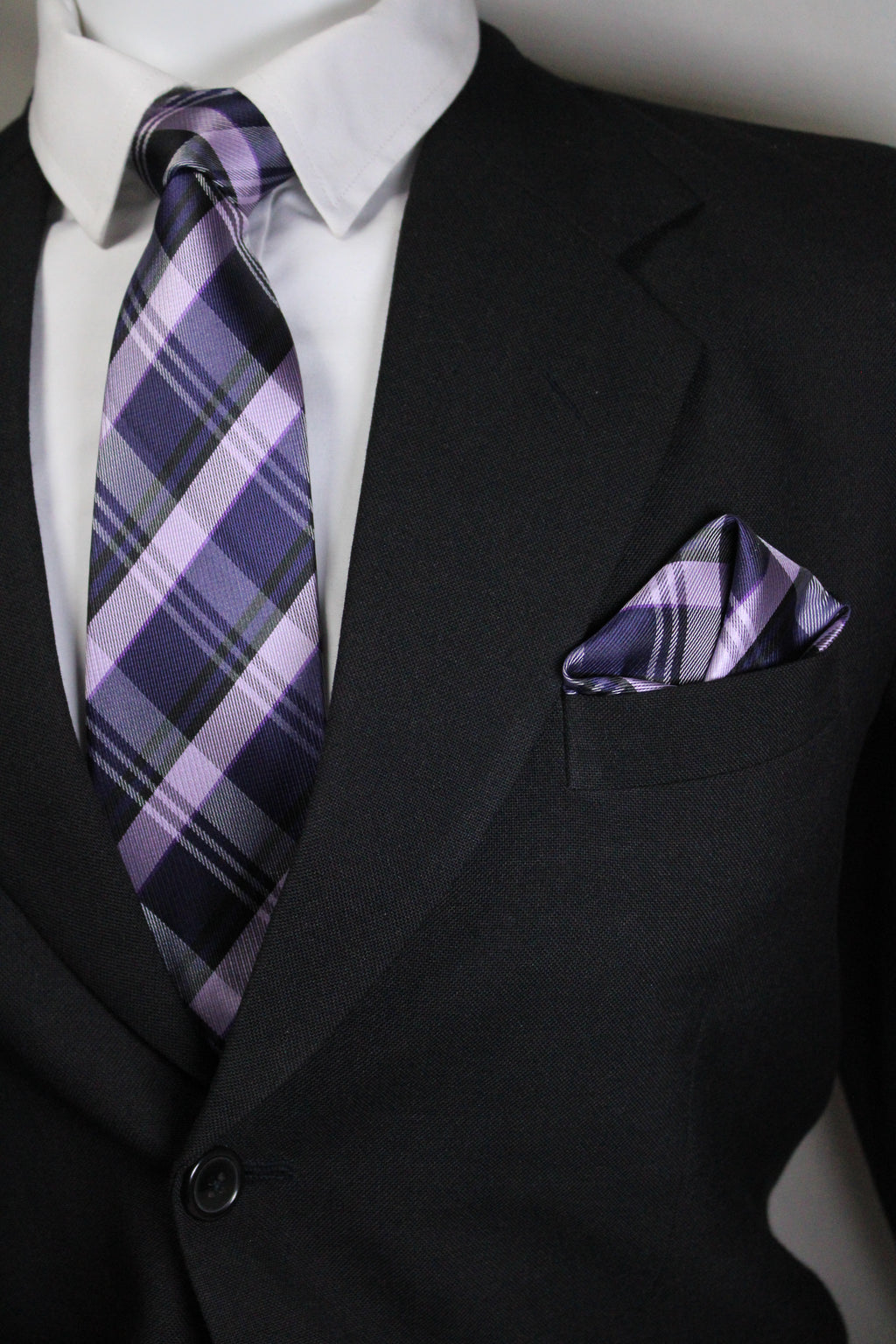 Close-up of a black suit with a purple plaid tie and pocket square Tie Benon