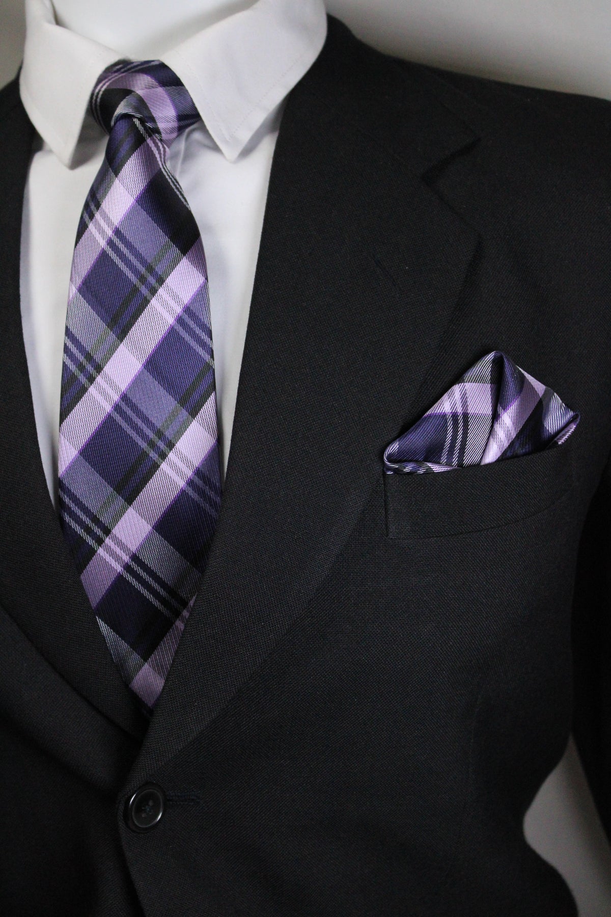 Close-up of a black suit with a purple plaid tie and pocket square Tie Benon