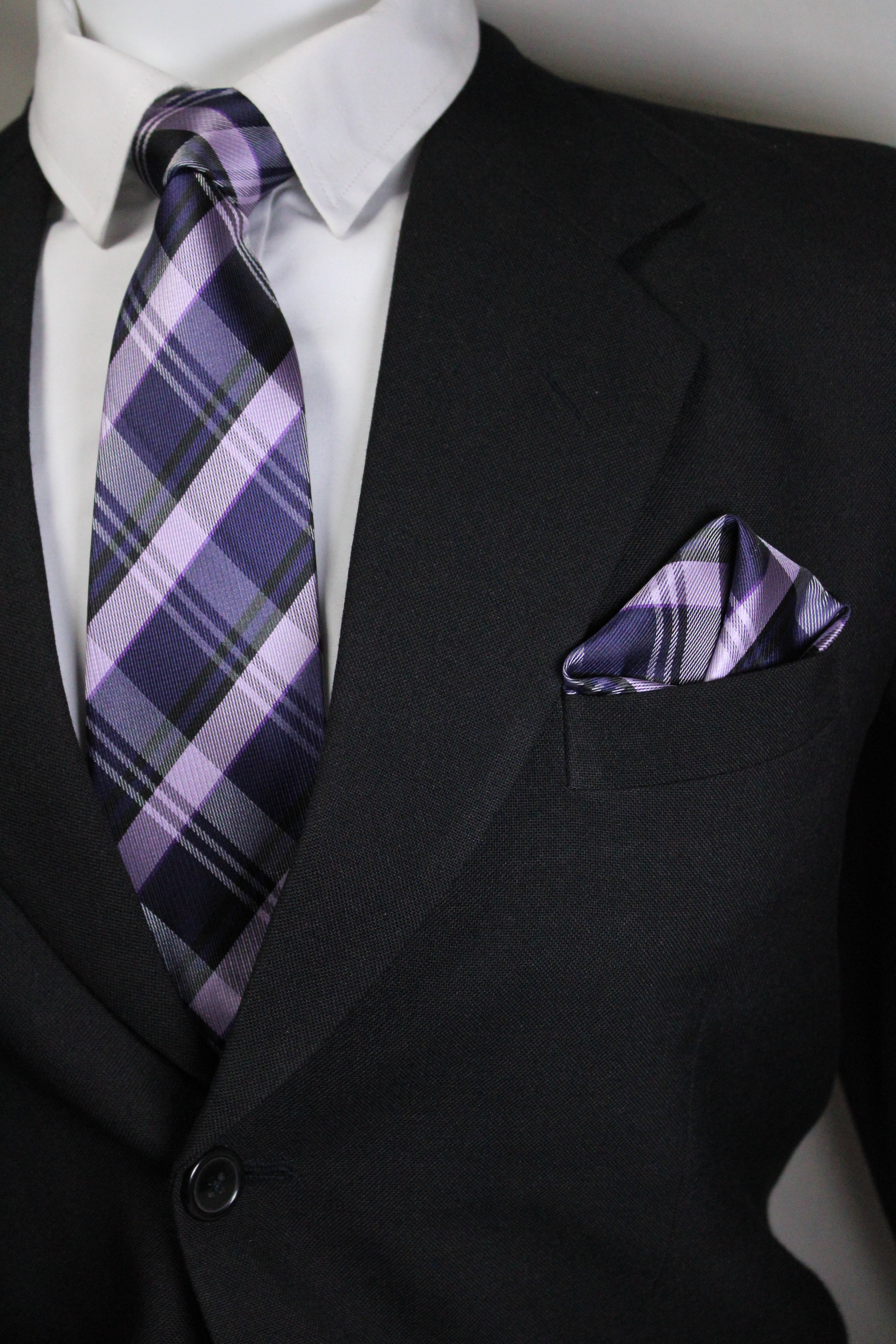 Close-up of a black suit with a purple plaid tie and pocket square Tie Benon