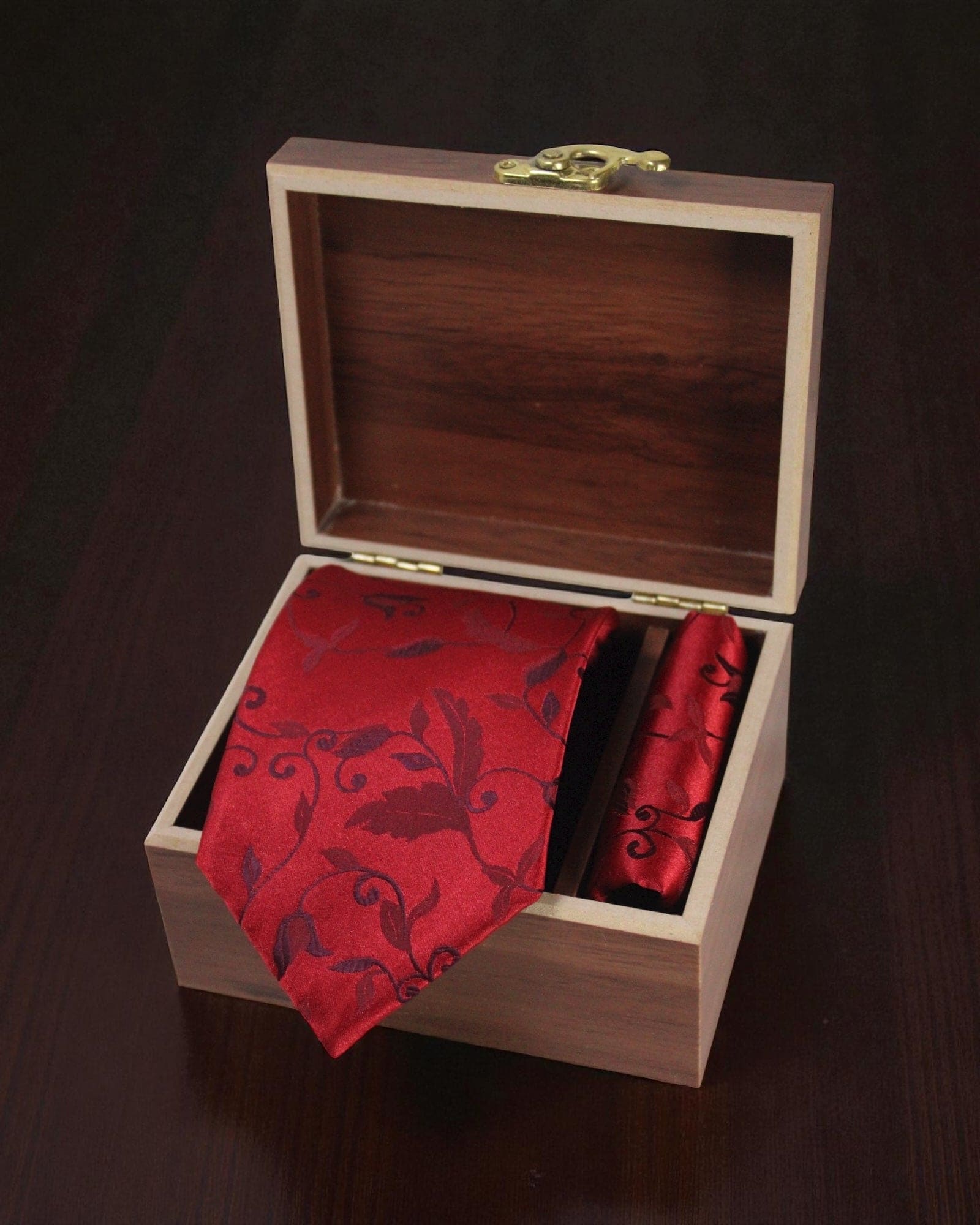 Red patterned tie and handkerchief in a wooden box on a dark surface