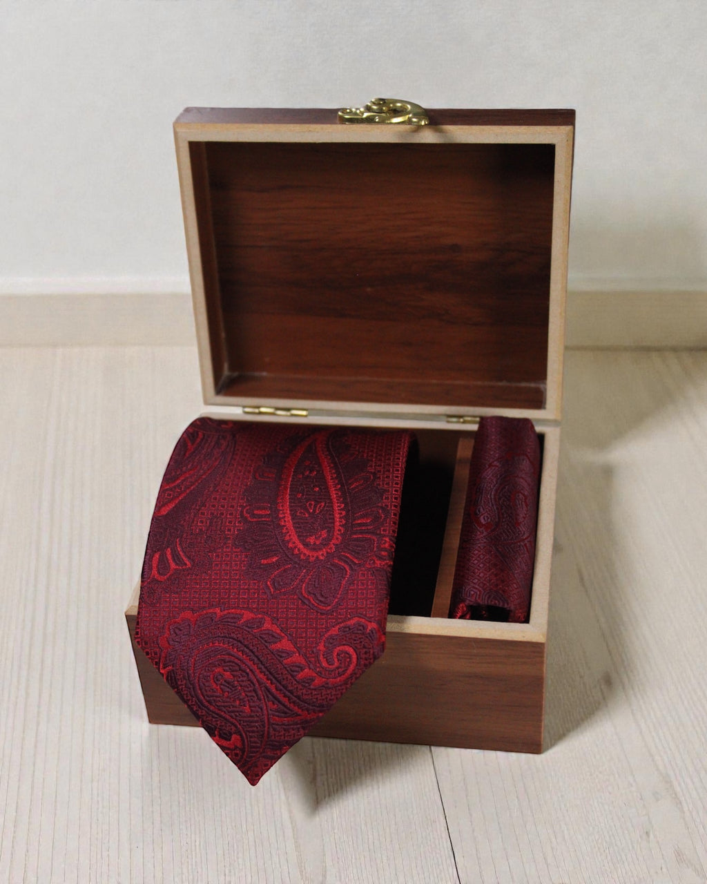 Red paisley tie and pocket square in a wooden box on a light wooden surface.