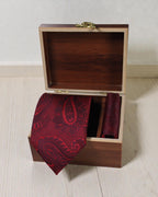 Red paisley tie and pocket square in a wooden box on a light wooden surface.