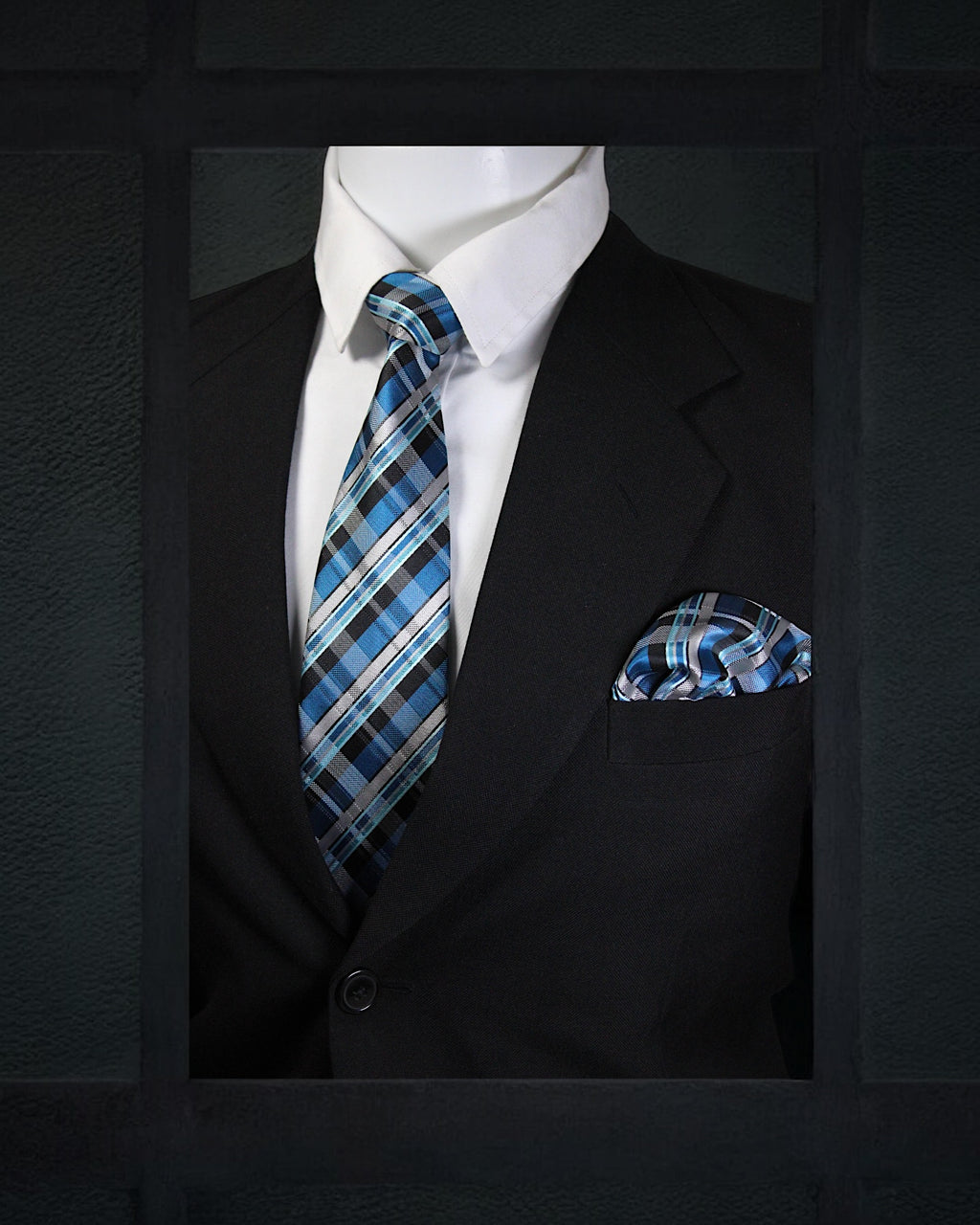 Mannequin wearing a black suit with a blue plaid tie and pocket square against a dark background