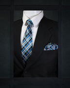 Mannequin wearing a black suit with a blue plaid tie and pocket square against a dark background