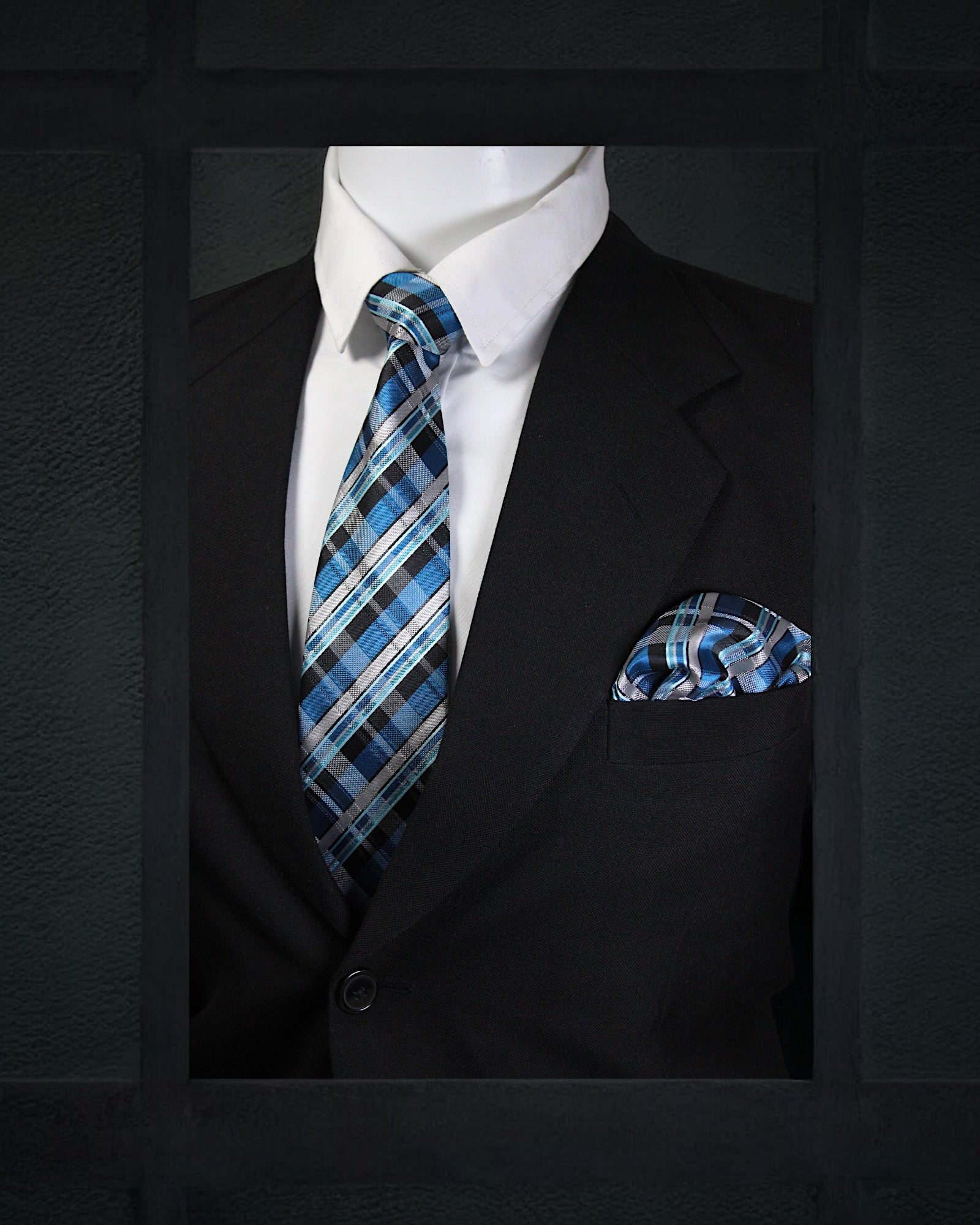 Mannequin wearing a black suit with a blue plaid tie and pocket square against a dark background