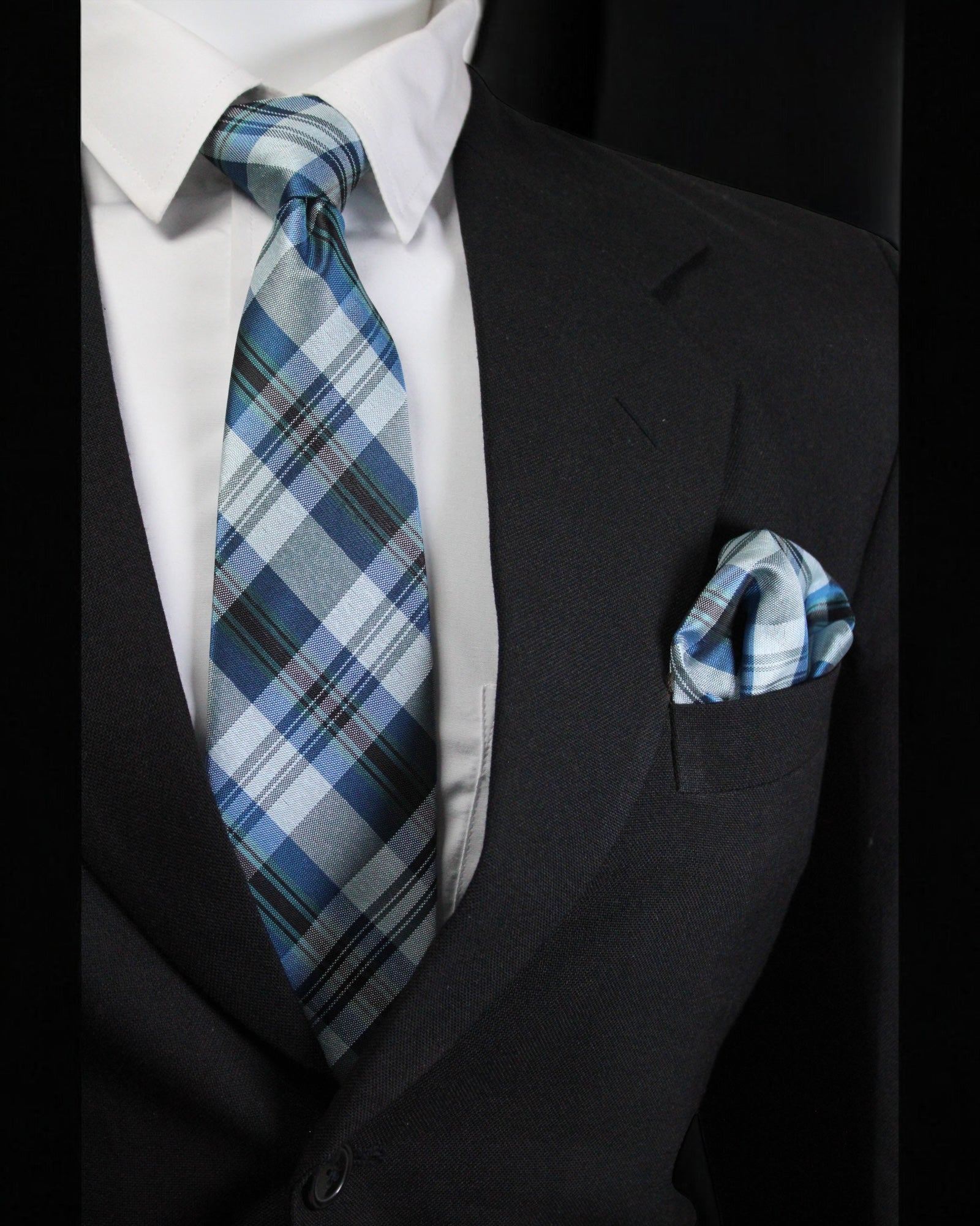 Man wearing a black suit with a white shirt, blue plaid tie, and matching pocket square Tie Benon