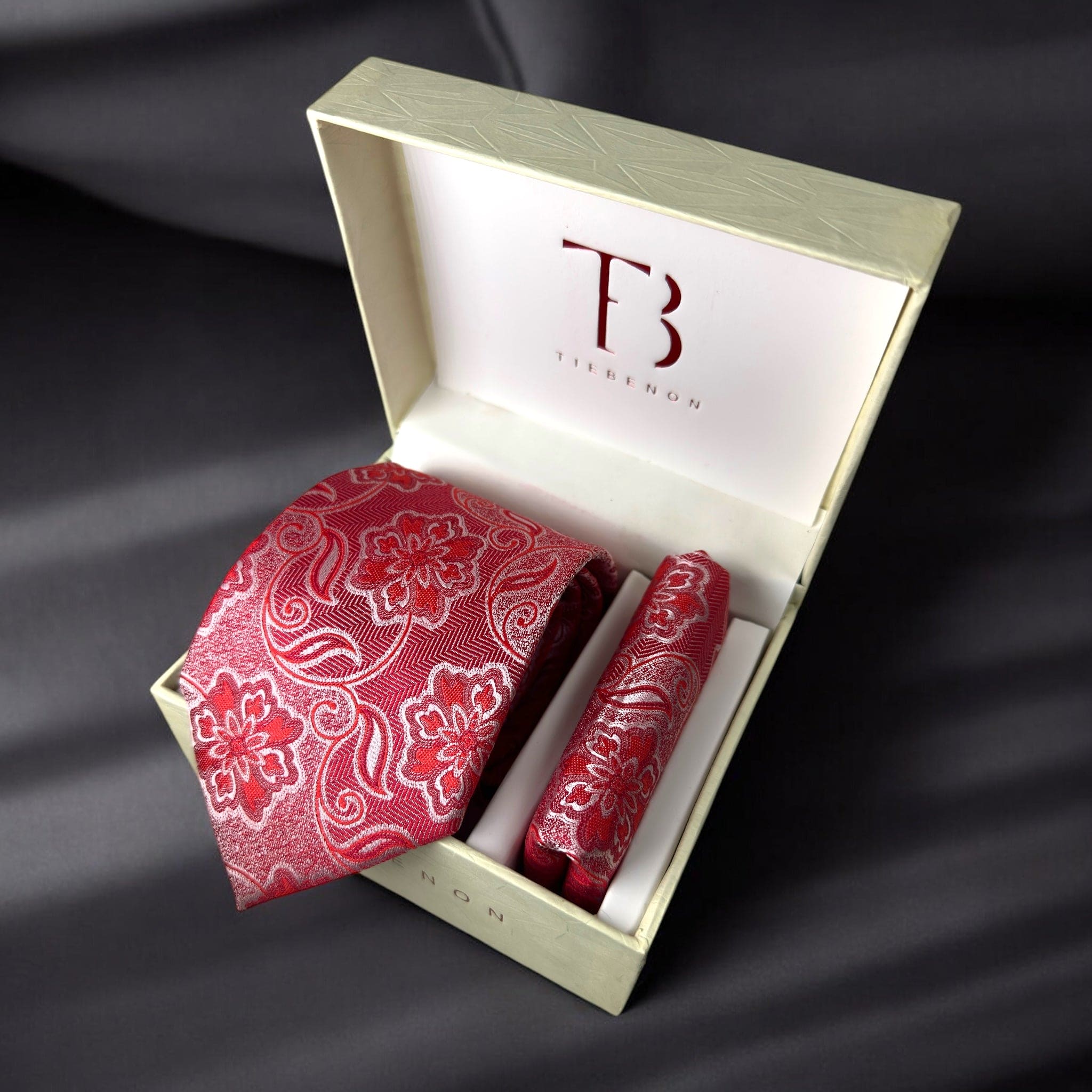 A red paisley tie with a pocket square, both laid out in a white box with a 'Tie Benon' branded cushion.