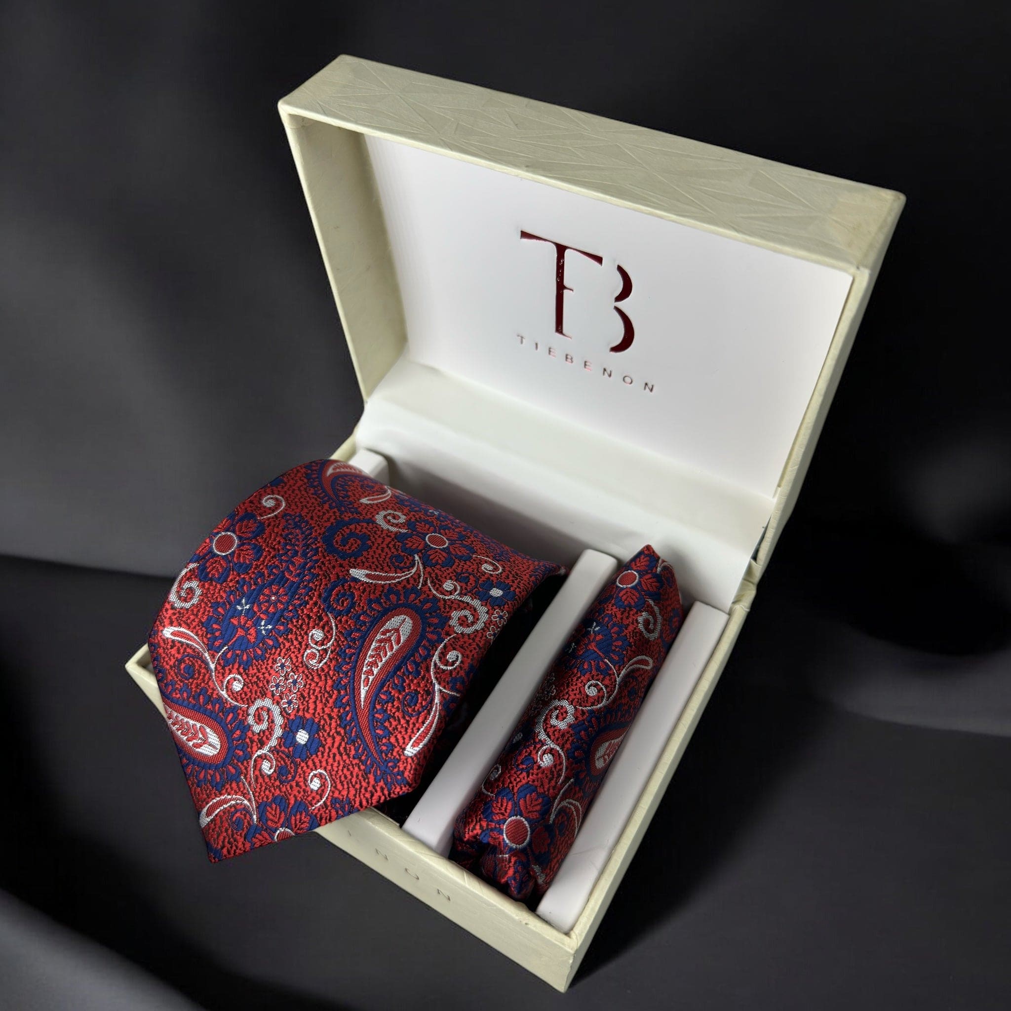 A Tie Benon branded red paisley tie with a pocket square, presented in an open wooden box with a dark interior.