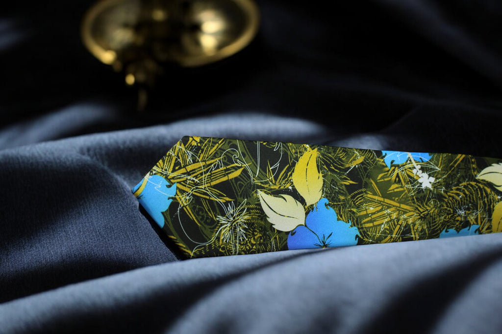 A floral tie with a deep forest green color and a pocket square, laid out on a surface with a blurred object in the background.