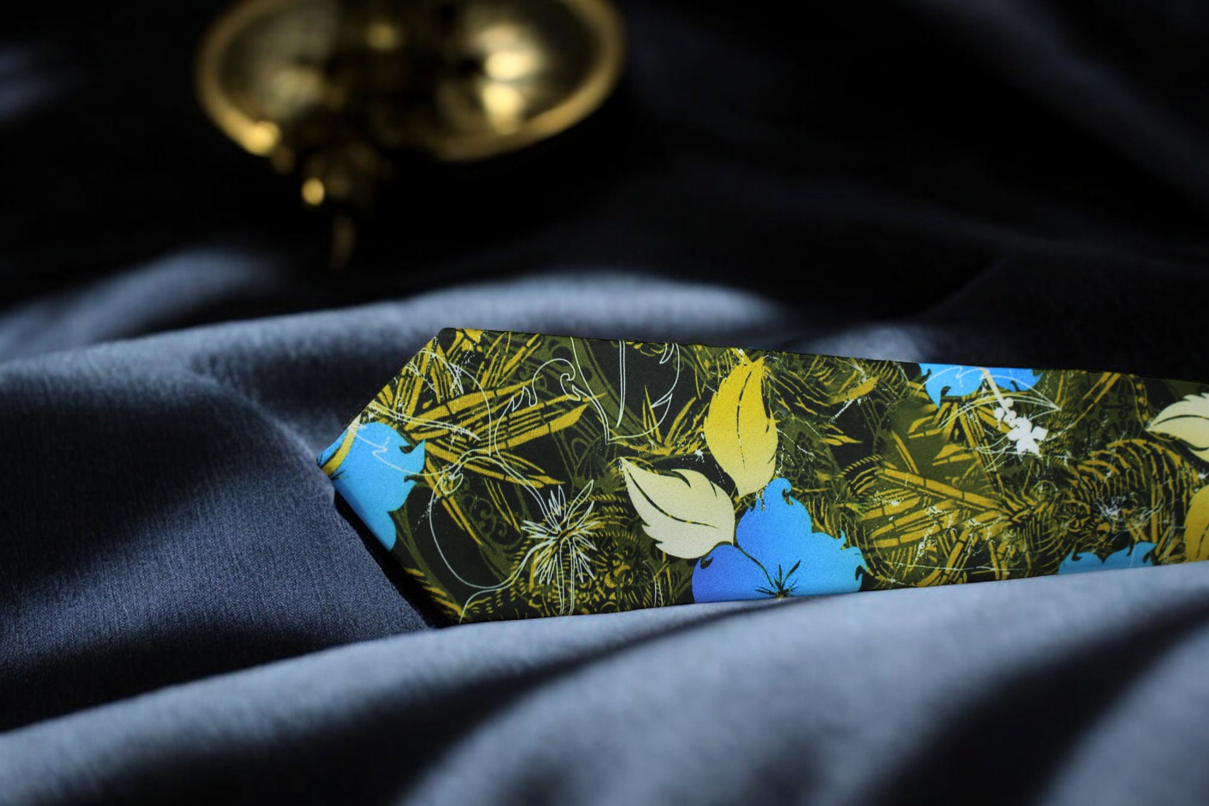 A floral tie with a deep forest green color and a pocket square, laid out on a surface with a blurred object in the background.