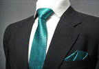 A turquoise geometric patterned tie and pocket square displayed on a mannequin wearing a black suit.