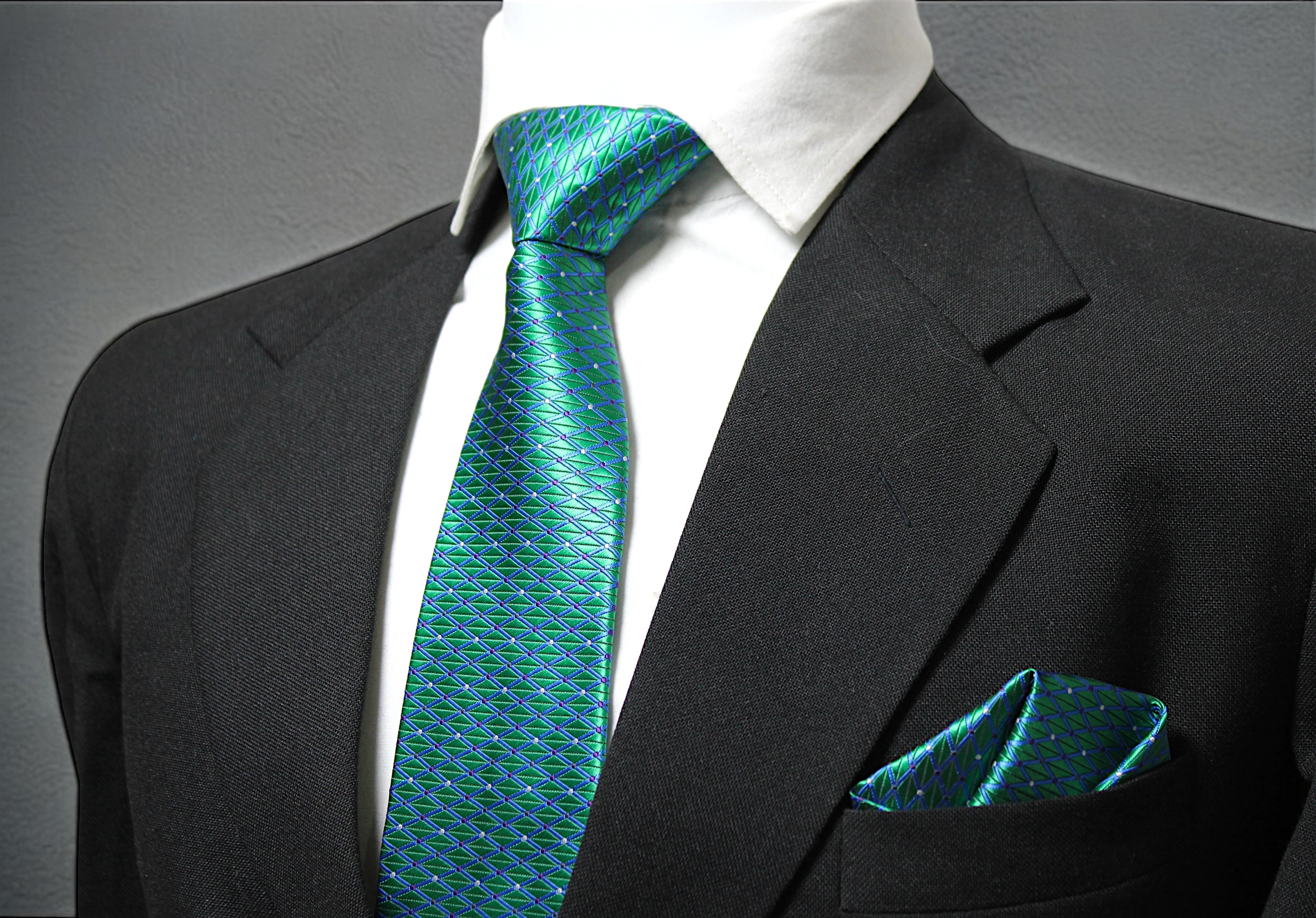 A turquoise geometric patterned tie and pocket square displayed on a mannequin wearing a black suit.