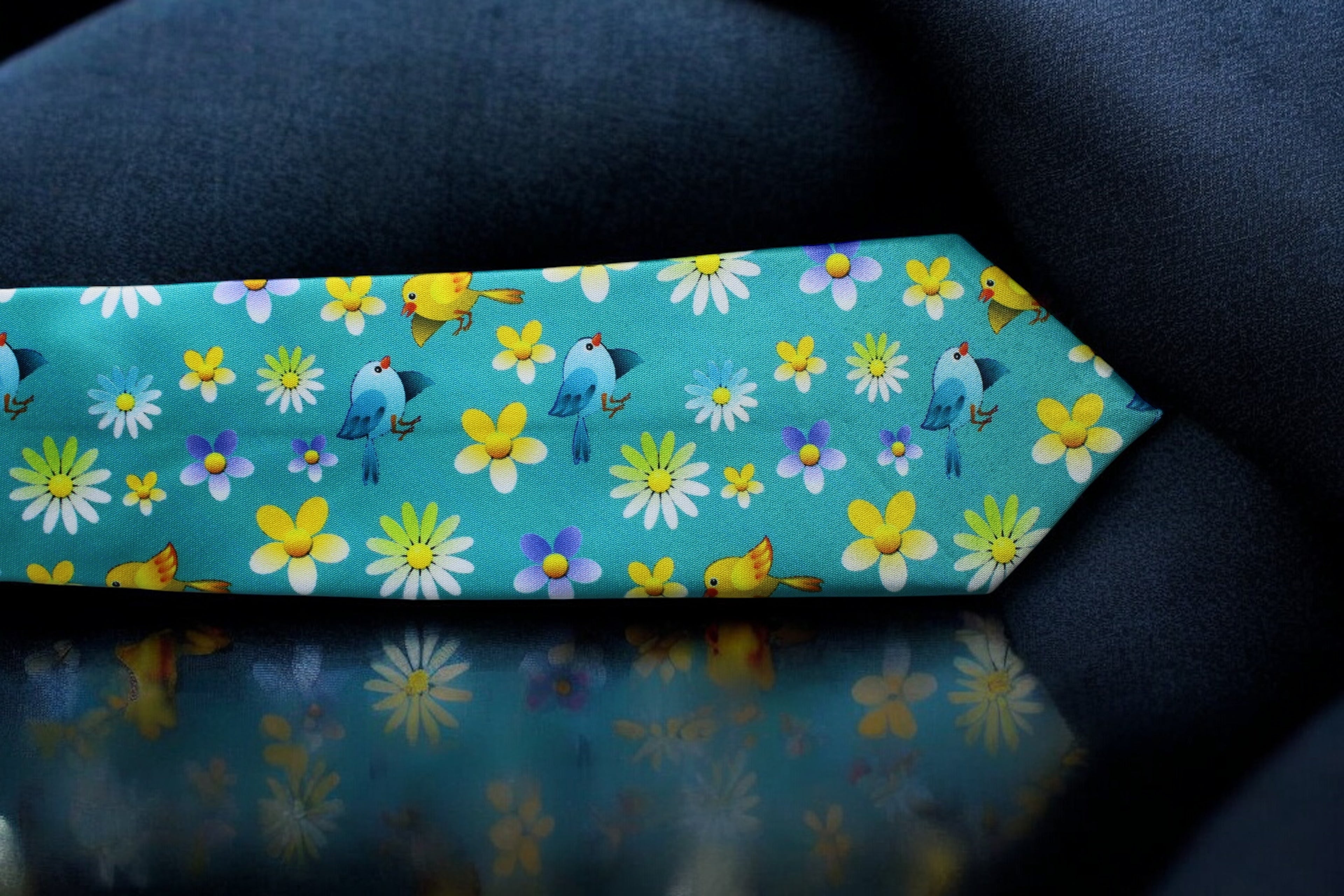 A turquoise necktie with a floral and bird pattern, displayed on a dark background.
